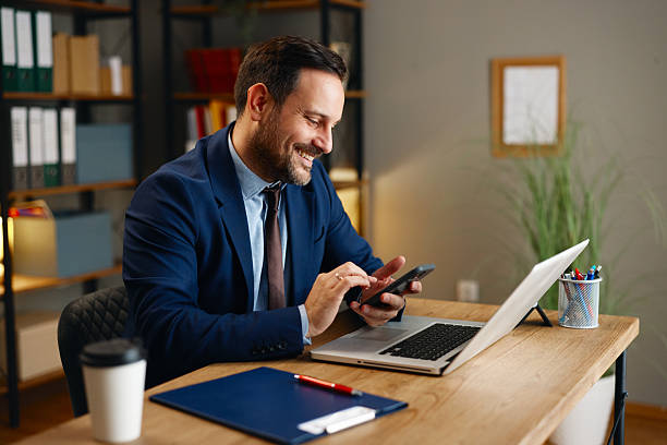 istock Smiling businessman using smartphone at desk in modern office 2254457405