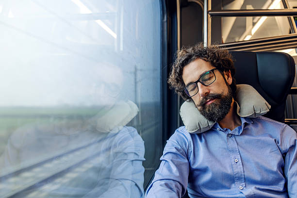Young adult man relaxing during a train journey with closed eyes, using a neck pillow to find comfort and rest while commuting or traveling for business purposes