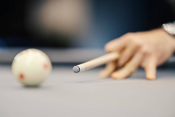 Player's hand guides cue stick for a precise shot on the cue ball at a pool table, close-up showing focus, concentration and skill during competitive indoor billiards game