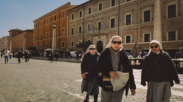 Catholic nuns walking along Via della Conciliazione, the main avenue leading to Vatican City, in Rome, Italy. The image documents everyday street life in the Vatican area, showing religious figures moving through a historic urban setting surrounded by pedestrians, buildings, and public activity.