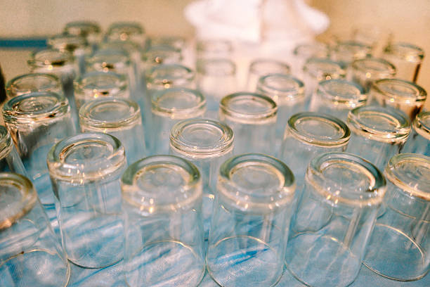 Numerous clean, empty glass tumblers are neatly arranged upside down on a light blue textured surface, reflecting soft light. This image suggests organization and readiness for use.