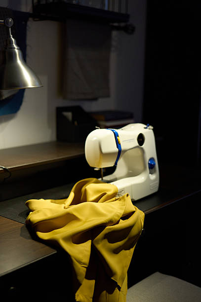 Sewing machine working on yellow fabric in a dimly lit workspace