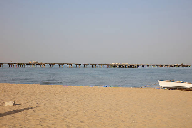 A tranquil coastal scene at sunset featuring Swakopmund Pier stretching into calm blue water, with sandy dunes in the distance. Ideal for travel, landscape, and desert-cocean contrasts.