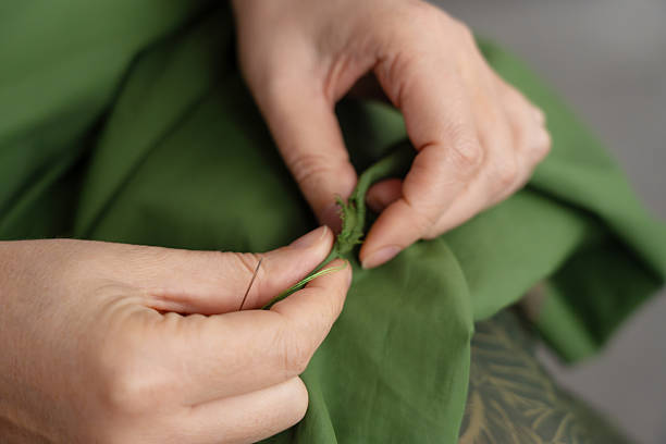 istock Woman darning a green jacket by hand with needle and patch fabric 2254467635