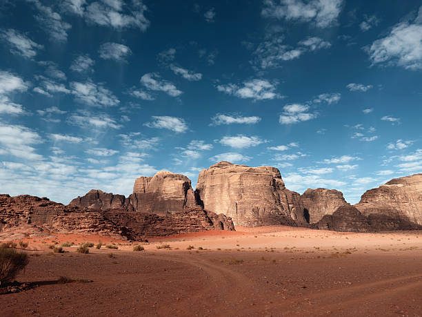 Jordan Wadi Rum Desert. Scenic landscape of Wadi Rum Desert with its famous Sandstone Mountains, Red Sand spotlit Sandstone Rocks and a bright dark blue sky filled with clouds. Mars-like Natural Desert Landscape. Wadi Rum, Southern Jordan - Border to Saudi-Arabia, Middle East