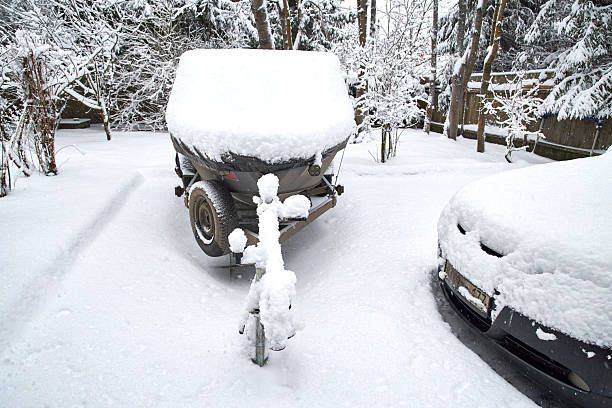 Boat on a trailer covered with thick snow in a winter yard. Abandoned watercraft standing outdoors in cold weather, completely buried under fresh snowfall in a quiet rural setting