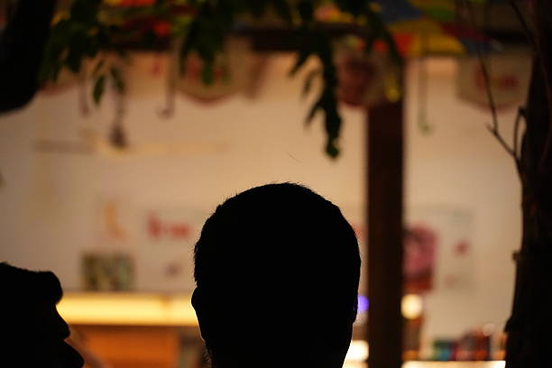 A dark silhouette of a human head from behind, set against a softly blurred background with colorful hints.