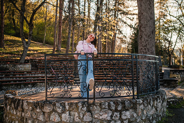 A beautiful smiling woman is standing leaning on a fence in nature and enjoying a beautiful sunny day