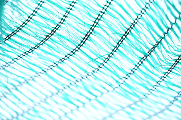 This image captures a vibrant turquoise mesh fabric with an abstract, wavy pattern. The strong backlighting emphasizes the texture and transparency, creating an interesting geometric design.