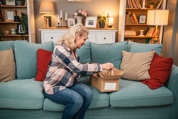 istock Smiling senior woman relaxing on sofa while unpacking cardboard box 2254476751