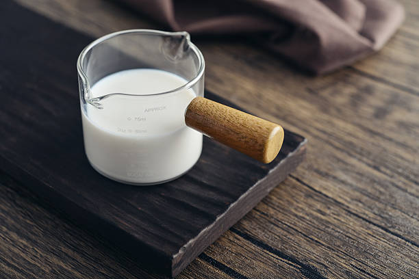 Milk in measuring glass cup with wooden handle on wooden background closeup