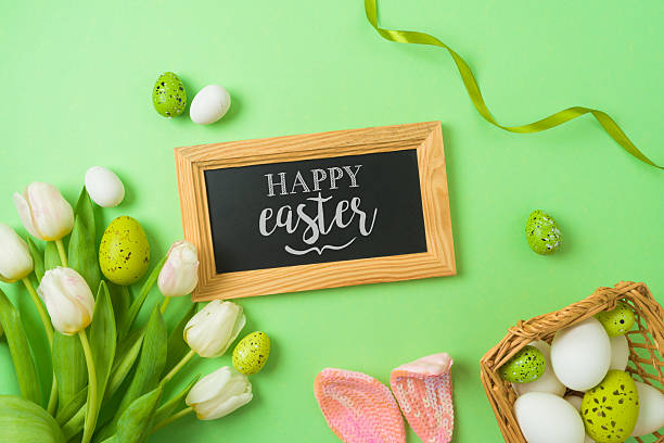 istock Easter holiday greeting card with chalkboard, easter eggs, basket and white tulip flowers on green background. Top view, flat lay 2254481346