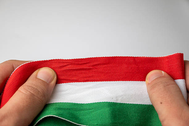 Close-up of hands holding a red, white and green fabric ribbon inspired by the national colors of Hungary. The image is suitable for advertising, design, cultural and promotional use.