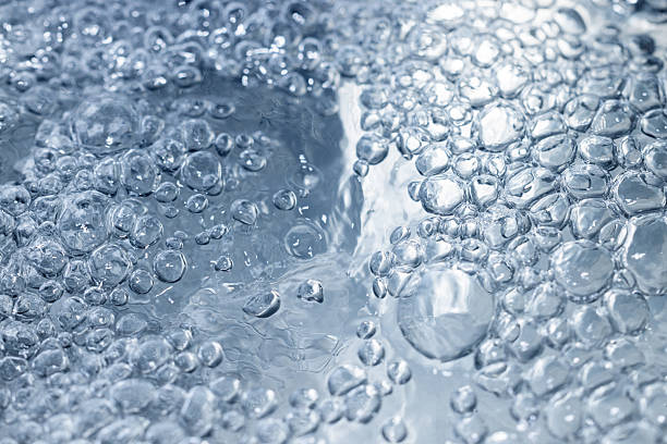Macro shot capturing numerous air bubbles suspended in clear blue water, creating a dynamic textured surface with shimmering light reflections. Ideal for freshness, cleanliness, water, and motion themes.