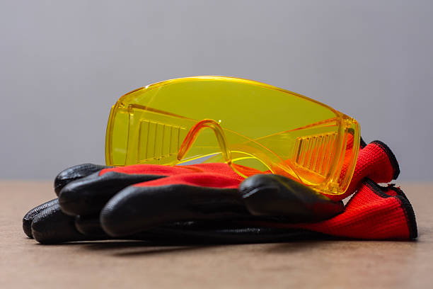 Yellow protective safety goggles black work gloves on wooden surface. Personal protective equipment for construction, repair, industrial work and workplace safety