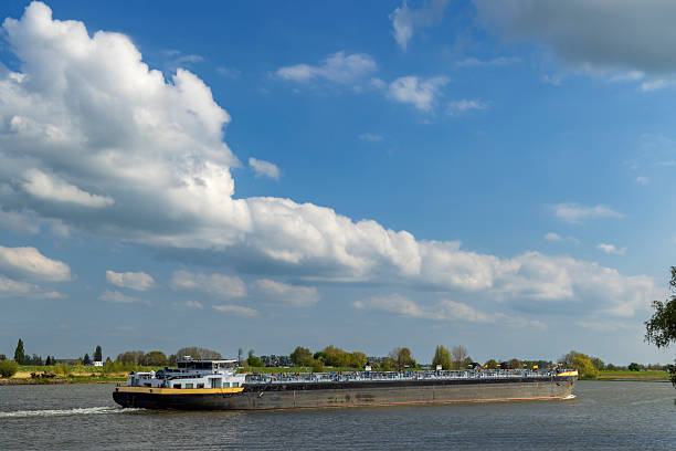 Tanker ship moving on a river under a blue sky with white clouds, Lekdijk West, Netherlands
