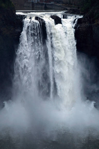 Snoqualmie Falls, a powerful waterfall located in Washington State, USA. Dramatic flow of water cascading over rocky cliffs, surrounded by evergreen forest and mist. Natural landmark, scenic landscape, travel and nature concept.