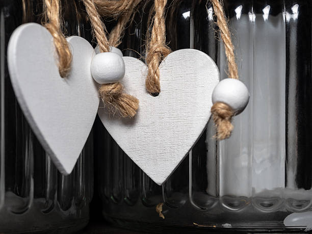 Rustic decor featuring white wooden heart shapes suspended by twine strings inside a glass bottle, creating a charming, romantic vignette perfect for Valentine's Day, home decor, or gift photography.