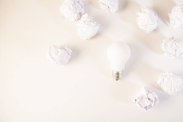 Light bulb surrounded by crumpled paper balls on white background.