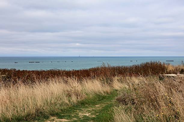 istock Pathway on the Normandy Coast with Remnants of Sunken Barges Offshore 2254507921