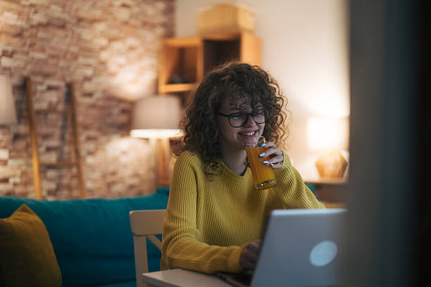 istock Woman drinking orange juice, using laptop at home 2254510881