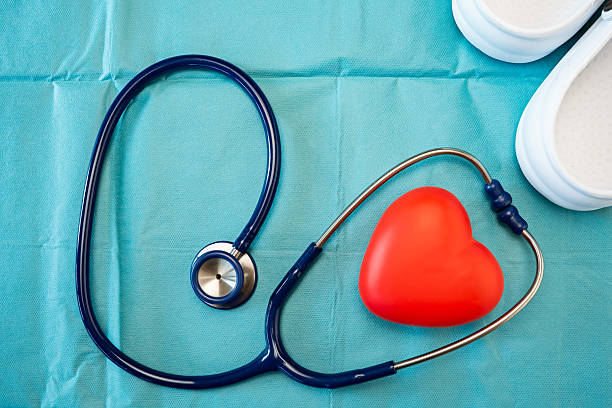 Stethoscope with red heart and medical clogs resting on blue surgical cloth representing cardiology and health control