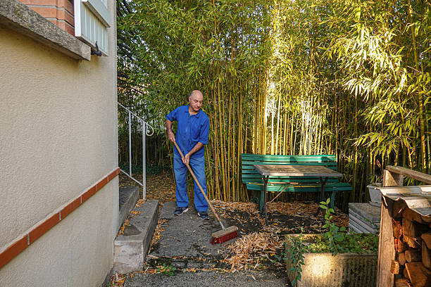 Man cleans leaves from concrete path in backyard space