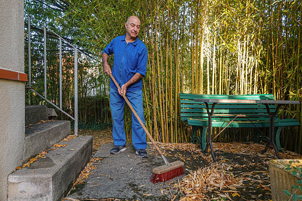 Man uses a broom to clean leaves in a terrace