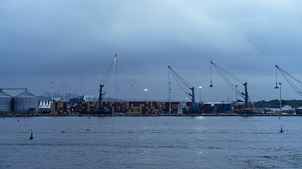Busy seaport at twilight, showing cargo containers, cranes, and grain silos