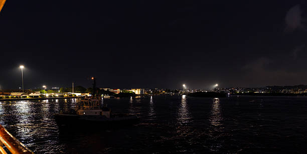 Tugboat moving on dark water at night with lights reflecting from the city
