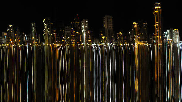 Urban skyline lights reflecting as abstract streaks over water at night