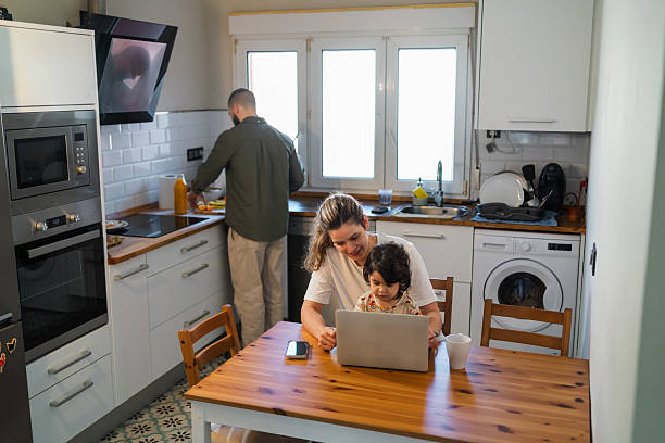 istock Young mother and child using laptop in kitchen while father cooks, balancing work and family life at home 2254520576