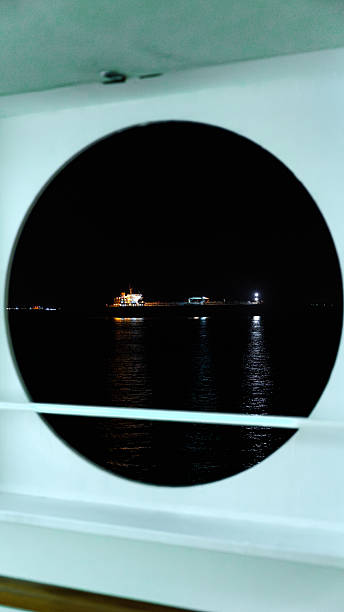 Ship with lights illuminating the water, seen through a porthole at night