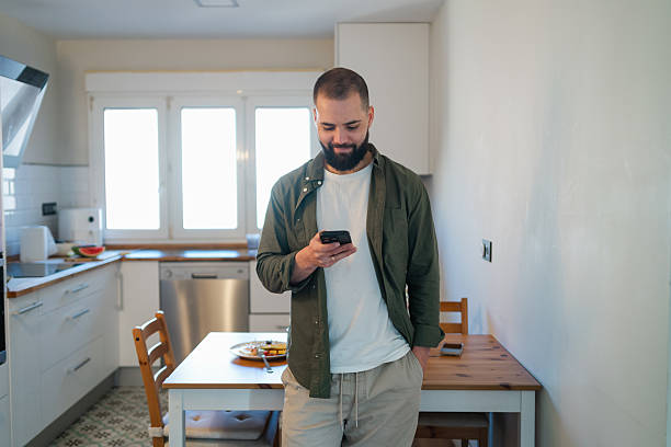 istock Man looking at device screen, enjoying technology in his modern kitchen setting with a clean, bright aesthetic 2254520813