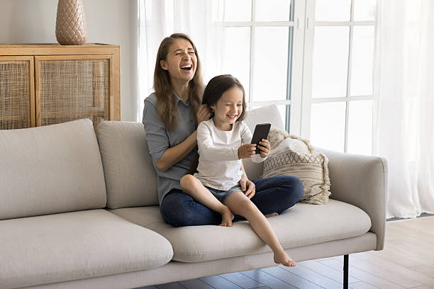 istock Kid and mom laugh sit on sofa with smartphone 2254520955