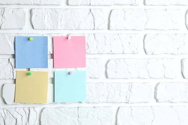 istock Colored paper stickers attached with pushpin on a white brick wall 2254523479