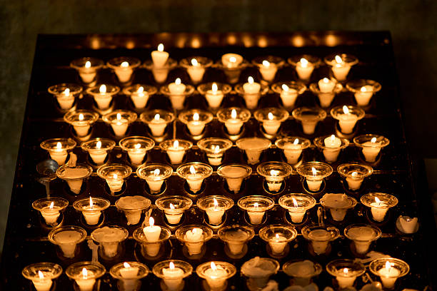 istock Rows of burning white votive candles in glass holders casting a 2254525863