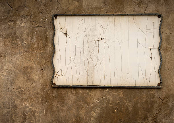 Close-up view of a weathered blank signboard mounted on a textured, cracked wall.