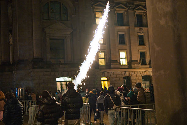 Berlin, Germany – January 1, 2026: A firework rocket is launched from a crowd near a historic building in Berlin during New Year celebrations. People stand behind barriers as sparks and smoke rise into the night sky.
