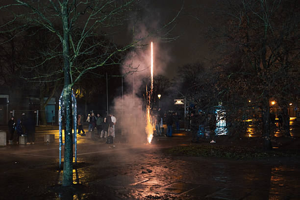 Berlin, Germany – January 1, 2026: A firework rocket rises vertically from a public square in Berlin during New Year celebrations. Smoke and sparks surround the launch area as people stand nearby in the illuminated urban environment at night.
