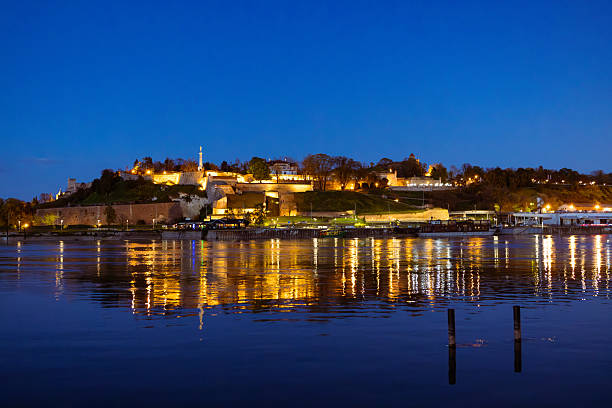 Beautiful night view of Belgrade Fortress illuminated and reflected on the calm waters of the Danube River under a moonlit sky.