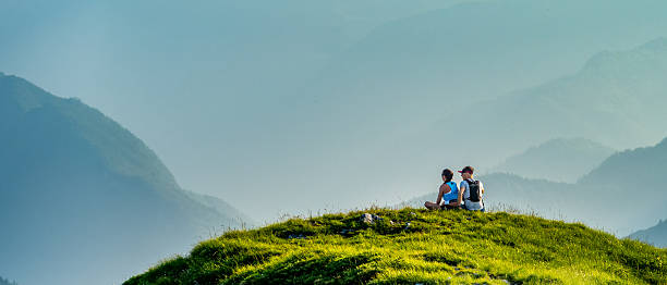 istock Two People Sitting on a Green Hill Overlooking a Misty Mountain Range 2254536108