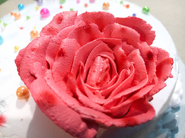Close up of a beautiful pink frosting rose on a white cake with sprinkles.