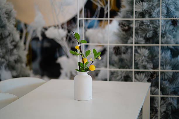 Fresh citrus branch in a white vase on a minimalist table with a soft background of pine trees creating a serene indoor atmosphere