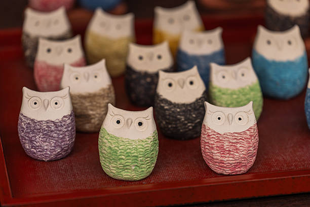 A charming collection of handcrafted ceramic owl figurines, each boasting a distinct textured, colorful body and a serene white head. These artisanal souvenirs, arranged on a red tray, evoke a sense
