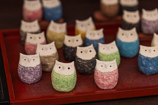 A charming collection of handcrafted ceramic owl figurines, each boasting unique textured bodies in vibrant colors and distinct white faces, neatly arranged on a rustic wooden tray. These delightful