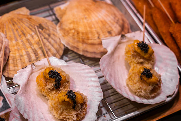 Close-up of delectable deep-fried seafood served in natural scallop shells, elegantly topped with rich sea urchin roe (uni) and glistening black caviar. A luxurious street food delicacy found in