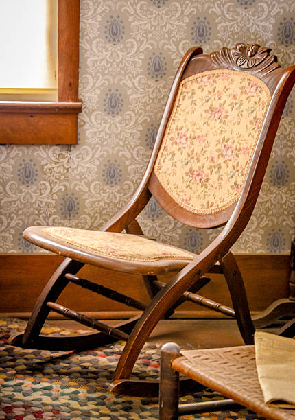 An old fashioned wicker chair rests on a braided rug beside a sunlit window and a small end table holding a paper lamp. The scene evokes warmth and nostalgia, suggesting slow mornings, handwritten letters, and the comfort of familiar spaces from years past.