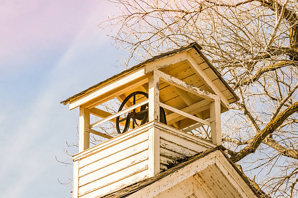 Looking upward at a steeple housing a school bell on an old fashioned one room schoolhouse. The simple structure and elevated perspective evoke a sense of history, tradition, and a time when a single bell marked the rhythm of the school day.