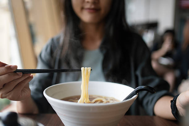 Person using chopsticks lifting Japanese udon noodles from a bowl of hot soup.